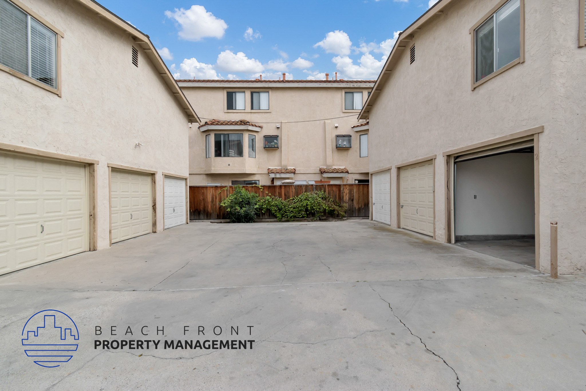 A large, empty parking lot in front of a two-story building with a logo for Beach Front Property Management in the bottom left corner.